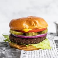 Side view of a single black bean burger on a bun, fully dressed, sitting on newsprint