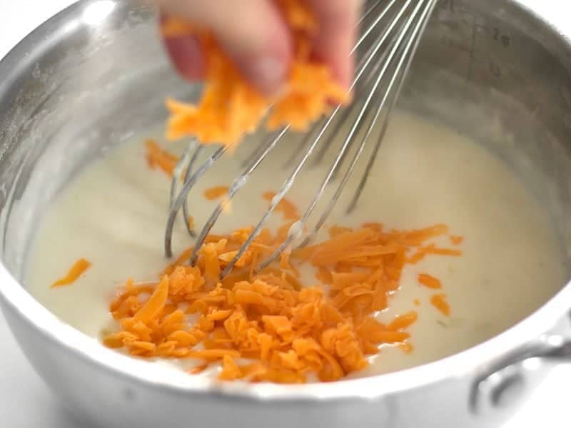 Cheddar cheese being added to pot with cheese sauce 