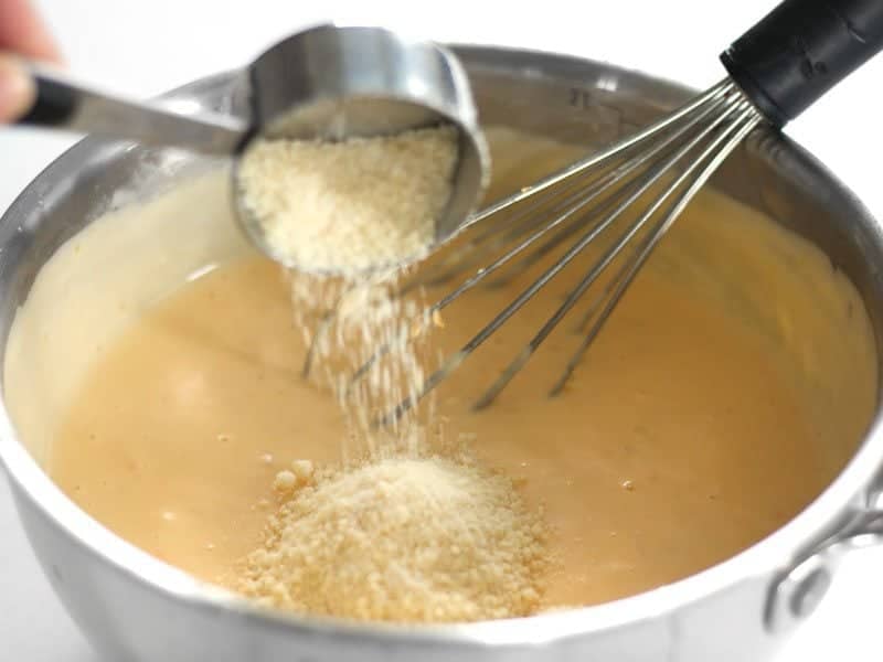 Parmesan being sprinkled into cheese sauce mixture 