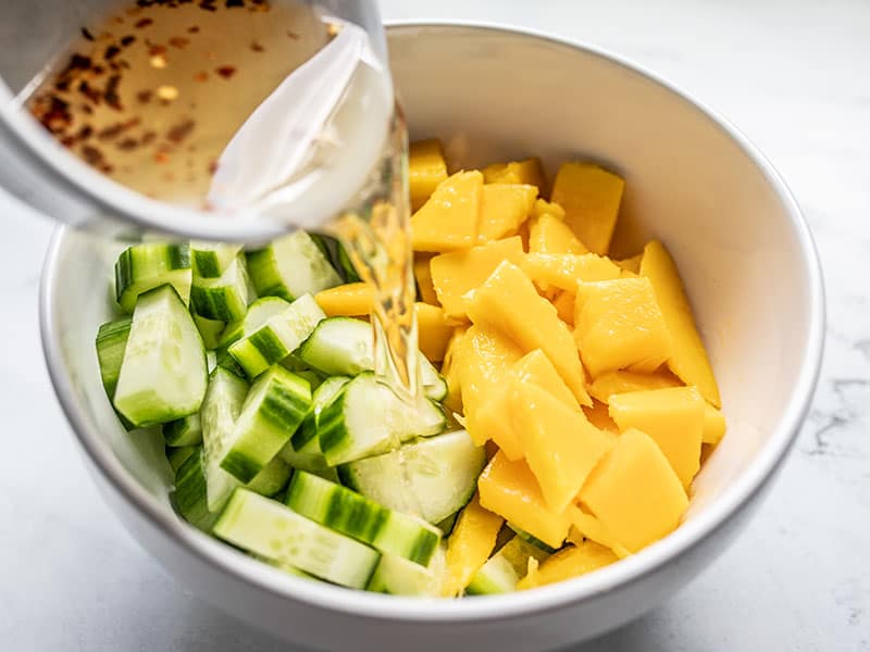 Dressing being poured over cucumber and mango in the bowl.