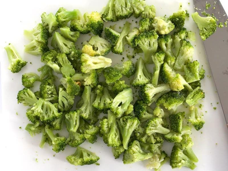 Frozen Broccoli Florets being chopped on cutting board with knife 