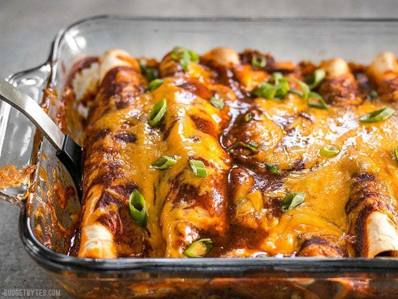 Side view of Chorizo and Sweet Potato enchiladas being lifted out of the casserole dish with a spatula