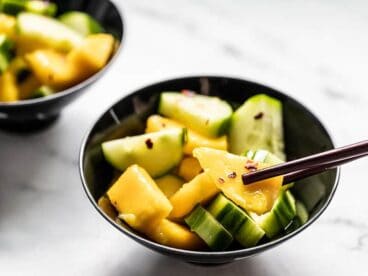 Close up of a bowl of cucumber mango salad with chopsticks picking up a piece of mango