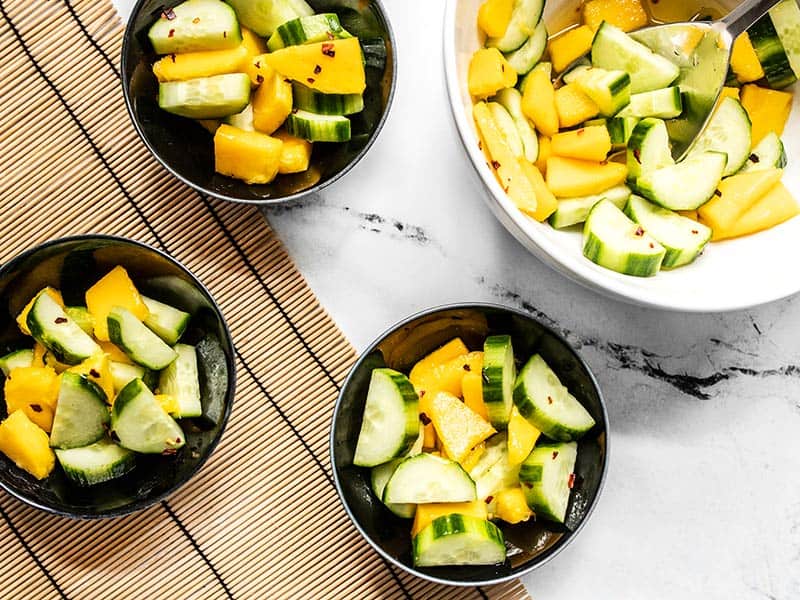 Cucumber mango salad being served into small black bowls from the large white bowl.