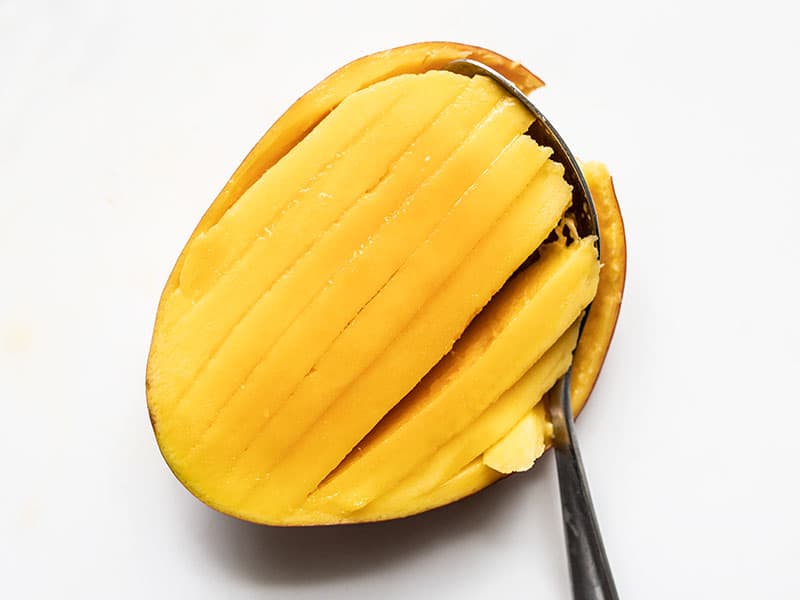 Mango flesh scored into slices with a spoon scooping them from the skin.