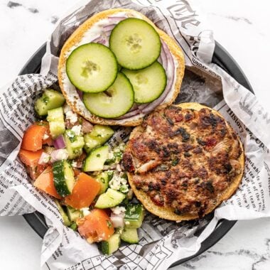 Overhead view of an open faced Mediterranean Turkey Burger on a paper lined plate with cucumber salad on the side