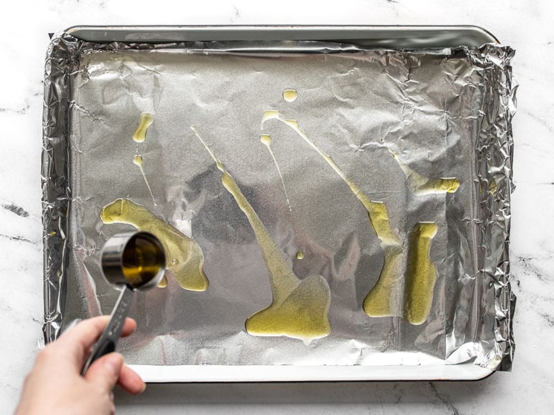 Olive oil being drizzled onto a baking sheet