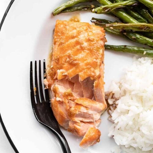 a flaked piece of baked ginger salmon on a plate with green beans and rice