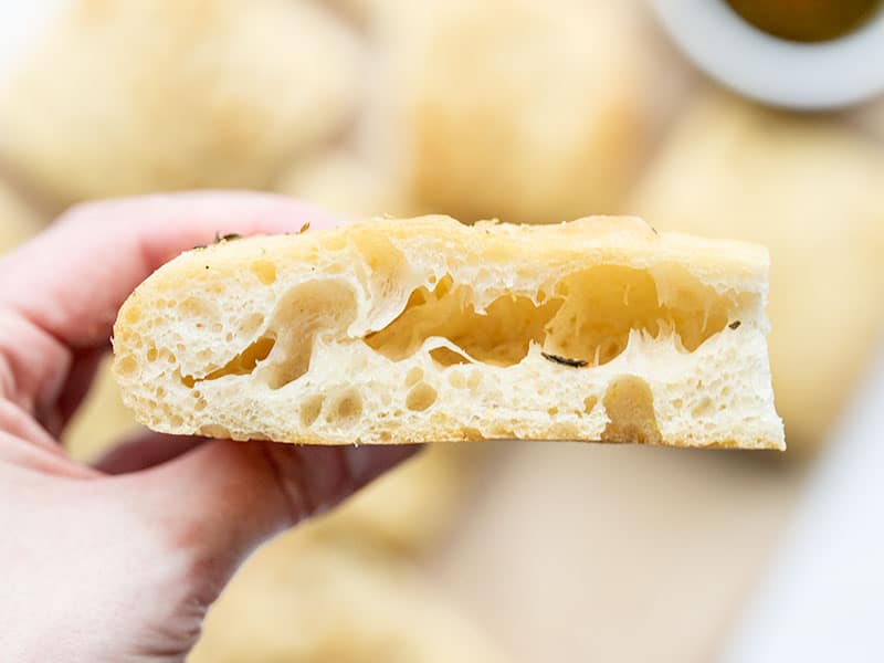 A hand holding a slice of focaccia so you can see the bubbles in the side