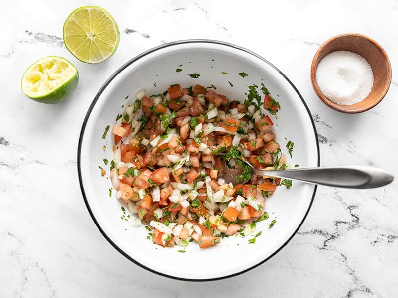 stirred pico de gallo in the bowl, salt and limes on the side