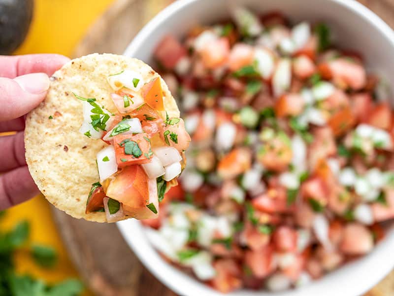 Close up of a chip topped with pico de gallo, the bowl in the background