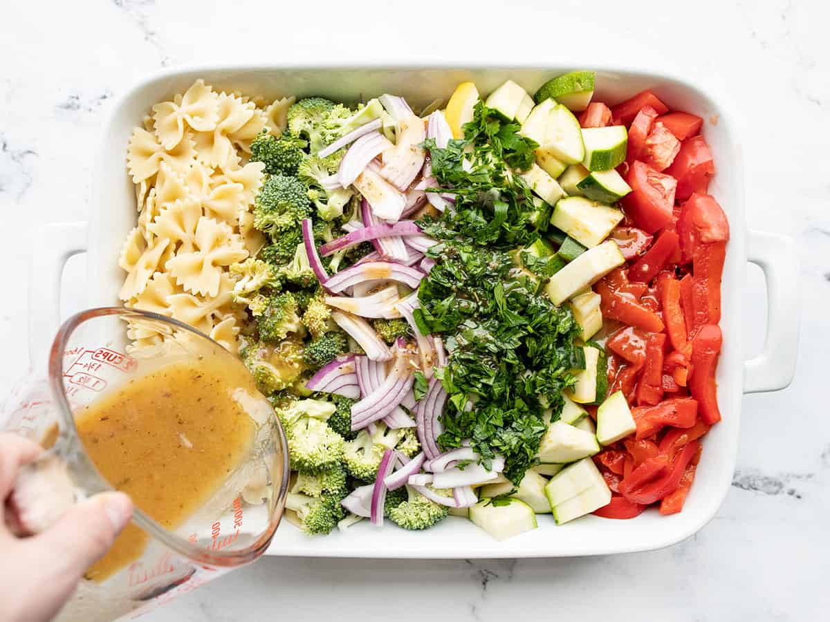 pasta and vegetables in a large dish, vinaigrette being poured over top