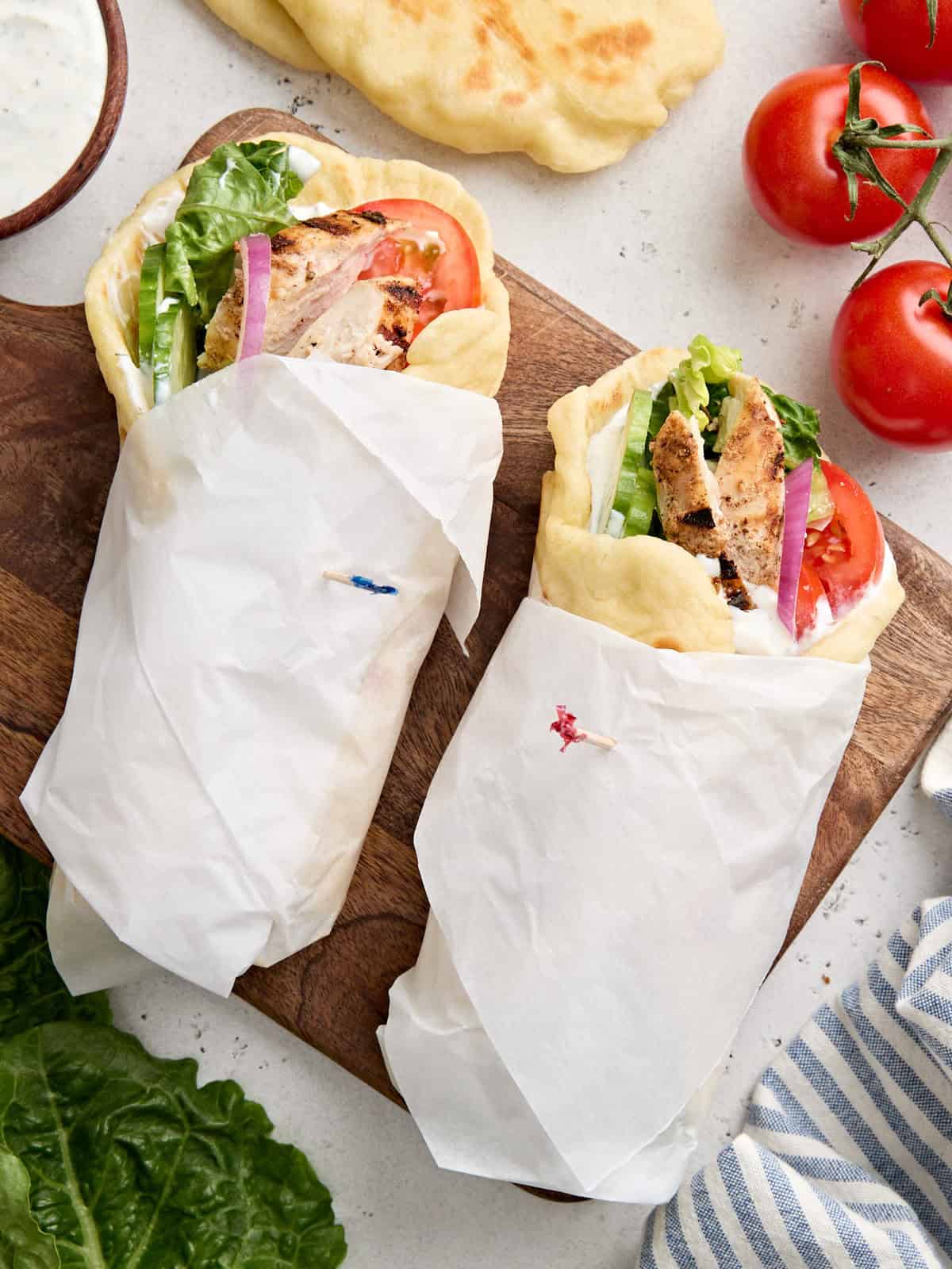 Overhead view of two chicken shawarma wraps on a wooden cutting board.