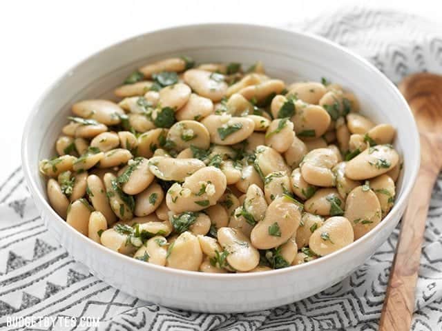 Marinated White Beans in white bowl with wooden spoon on the side 