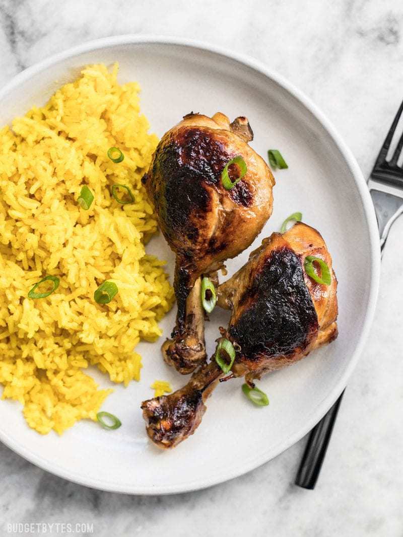 Two chicken adobo drum sticks plated on a white plate with a side of rice 