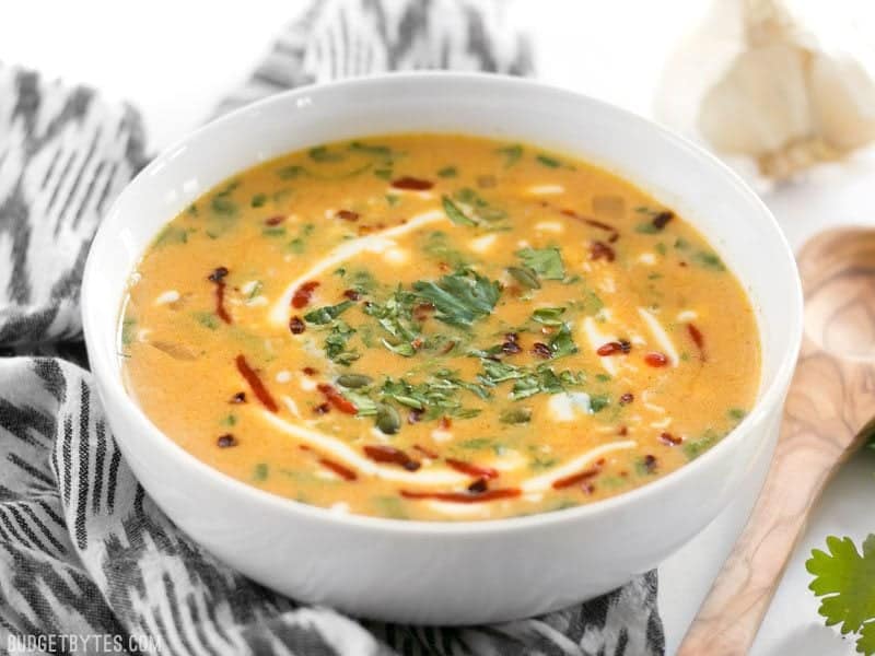 White bowl full of Spicy Coconut and Pumpkin Soup with wooden spoon on the side 