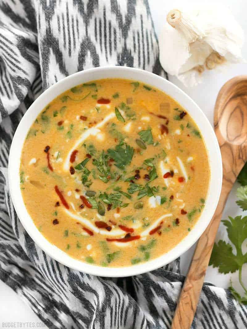 Top view of a bowl of Spicy Coconut and Pumpkin Soup in a white bowl with a wooden spoon on the side