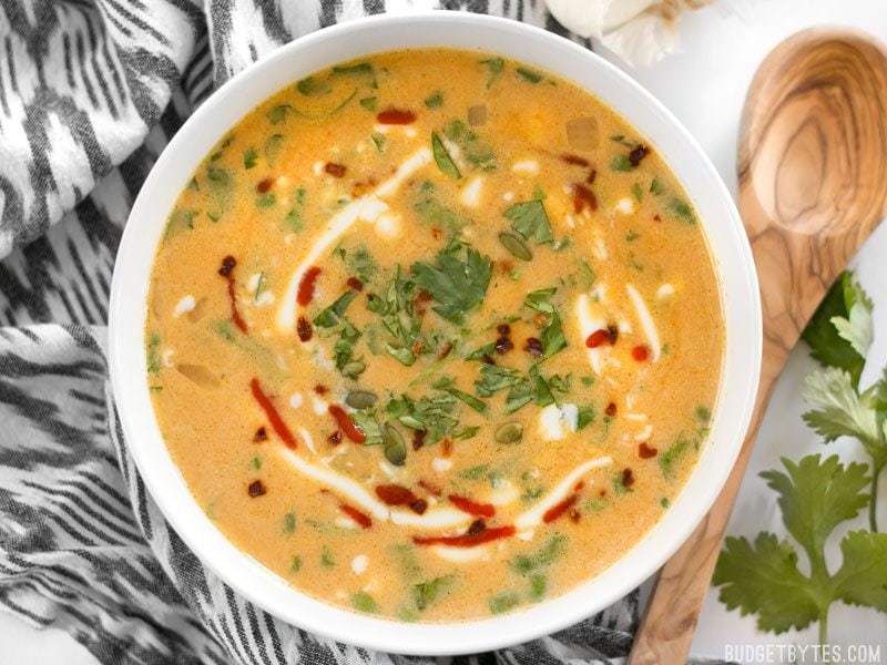 Top view of a white bowl of Spicy Coconut and Pumpkin Soup with a wooden spoon on the side