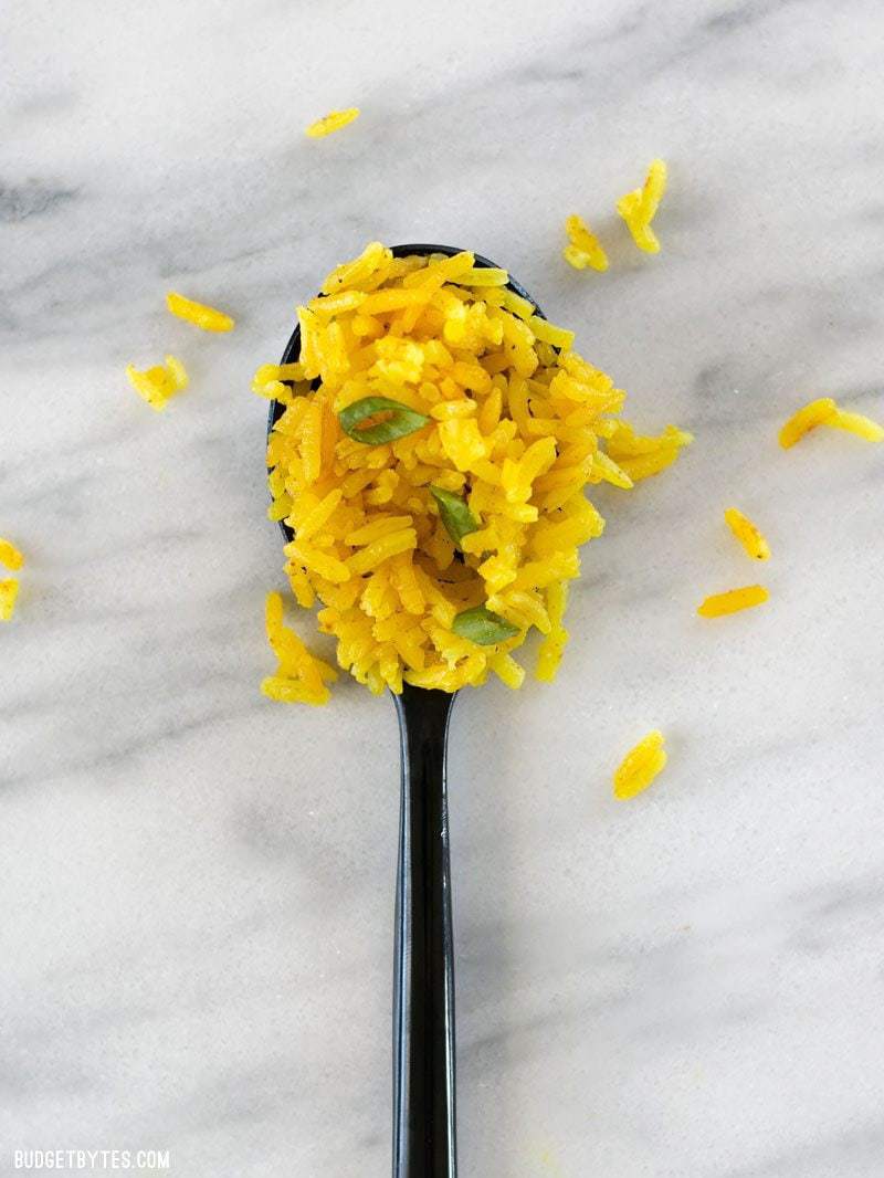 One spoonful of Yellow Jasmine rice on a marble countertop and a few grains scattered around. 