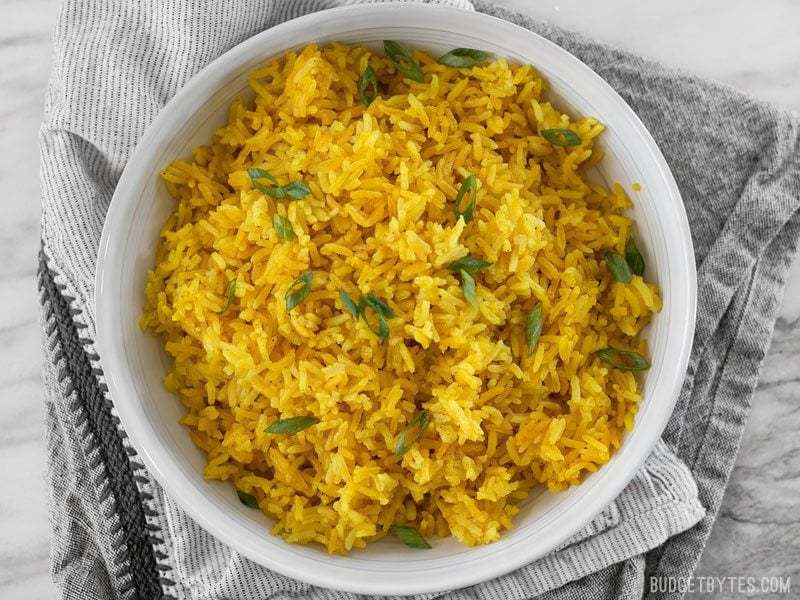 Bowl of finished Yellow Jasmine Rice with green onion sprinkled overtop and a grey napkin underneath. 