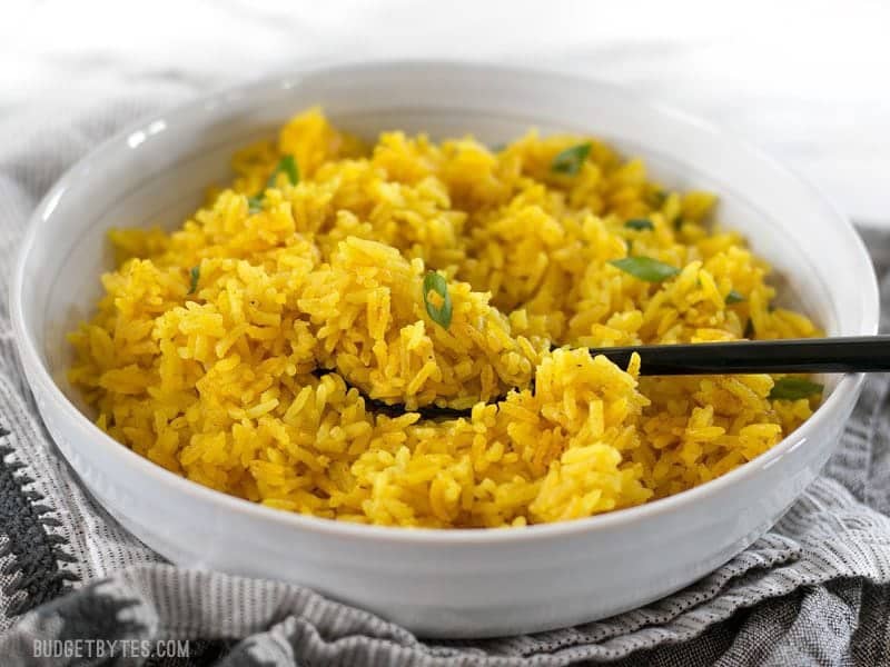 Front view of a white bowl full of Yellow Jasmine Rice and a black spoon.