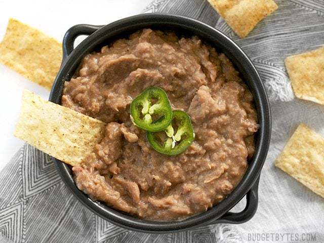 A chip being dipped into a bowl of slow cooker (not) refried beans with jalapeño garnish