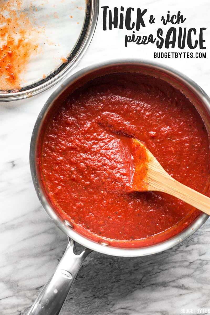 Overhead view of a pot full of Thick and Rich Pizza Sauce with the lid on the side and a wooden spoon in the pot.