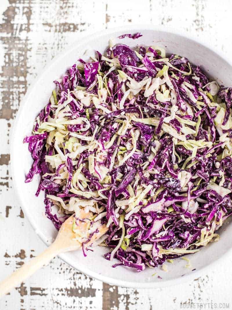 Top view of vinaigrette slaw with feta in white bowl with wooden spoon 