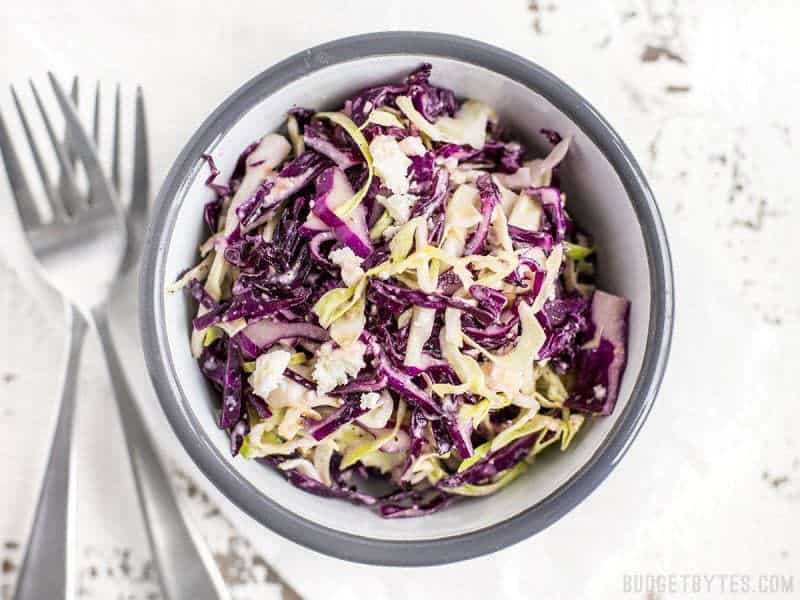 Top view of a bowl of vinaigrette slaw with feta with two forks on the side 