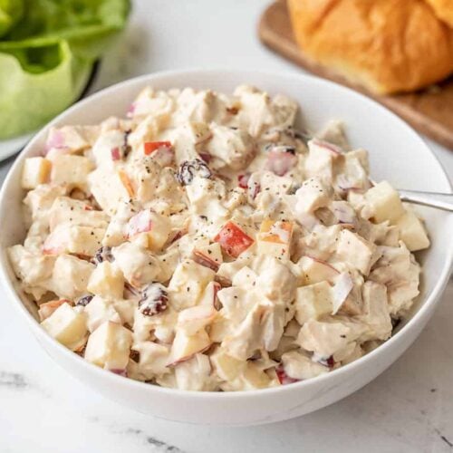 Side view of a bowl of chicken salad with apples, croissants in the background