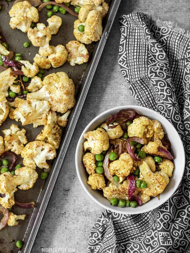 A bowl of Curry Roasted Cauliflower next to the roasting sheet pan.