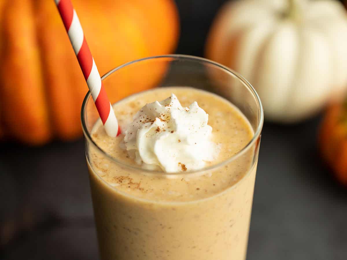 Side view of a pumpkin smoothie in a glass with a straw