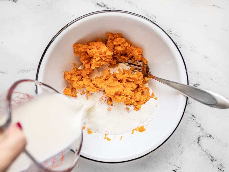 Milk being poured into the bowl with the mashed sweet potato
