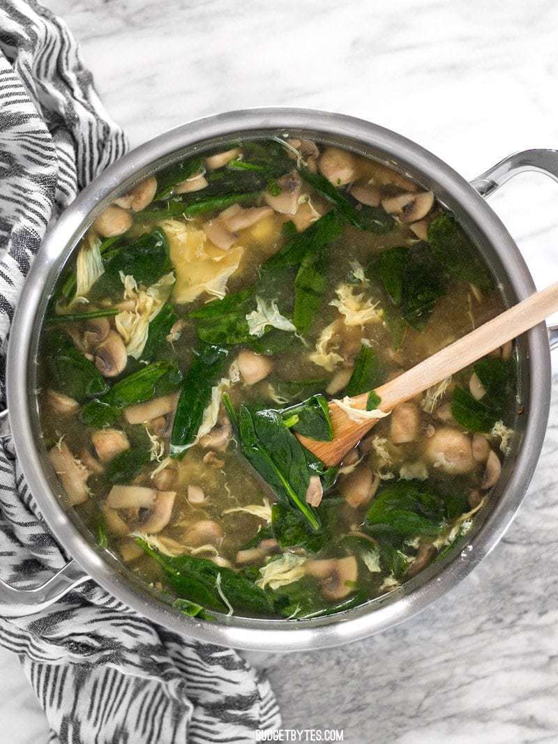 Overhead view of a large pot of homemade egg drop soup with spinach