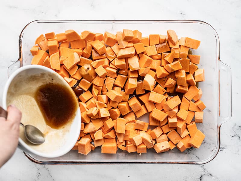 Butter mixture being poured over cubed sweet potatoes