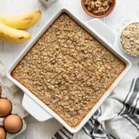 Overhead view of a casserole dish full of banana bread baked oatmeal, surrounded by ingredients