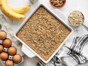 Overhead view of a casserole dish full of banana bread baked oatmeal, surrounded by ingredients