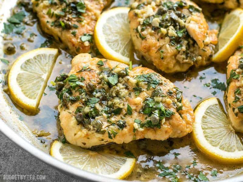 Close up of capers and parsley on top of a piece of Chicken Piccata with lemon garlic sauce.