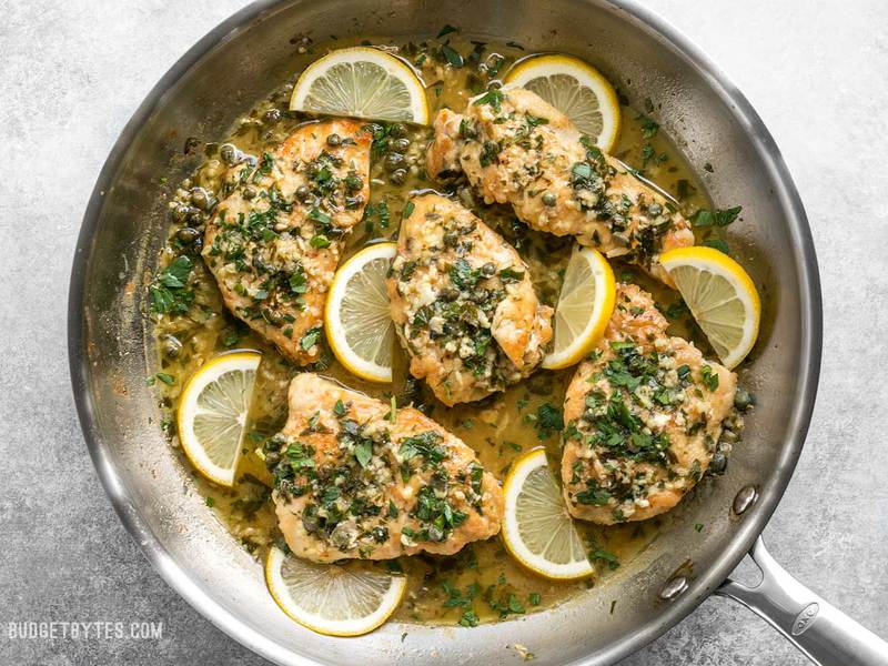 Finished Chicken Piccata in the skillet with parsley sprinkled over top and lemon slices scattered throughout.