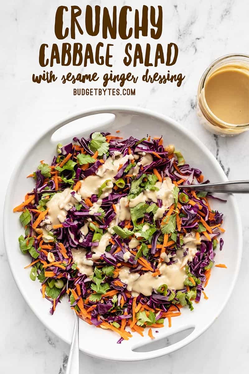 Crunchy cabbage salad in a white serving bowl with a jar of dressing on the side