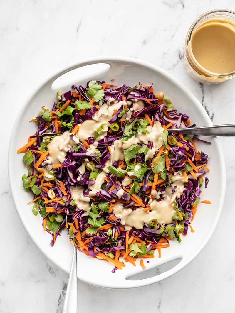 Crunchy Cabbage Salad in a white serving dish with two forks, drizzled with sesame ginger dressing