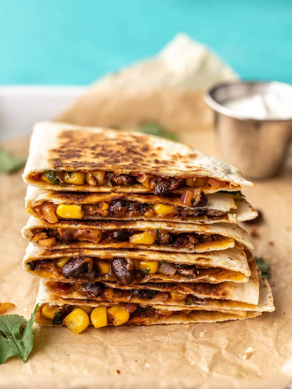 A stack of black bean quesadillas on a tray with a dish of sour cream behind them