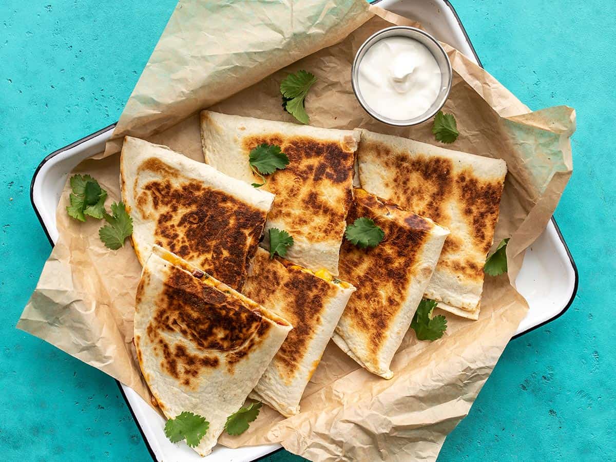 Overhead view of black bean quesadillas on a serving tray with a dish of sour cream