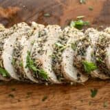 Slices of Herb Roasted Pork Tenderloin on a wooden cutting board.