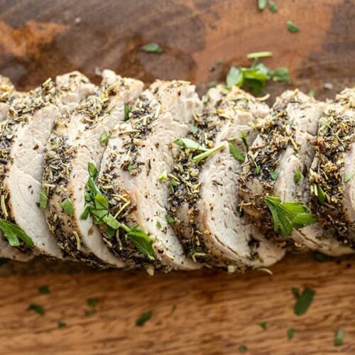 Slices of Herb Roasted Pork Tenderloin on a wooden cutting board.