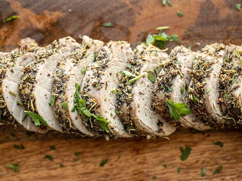 Slices of Herb Roasted Pork Tenderloin on a wooden cutting board.