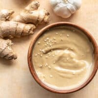 A wooden bowl filled with sesame ginger dressing next to a knob of fresh ginger