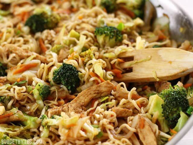 A close up view of the finished pan of Chicken Yakisoba with vegetables in the skillet with a wooden pasta fork.
