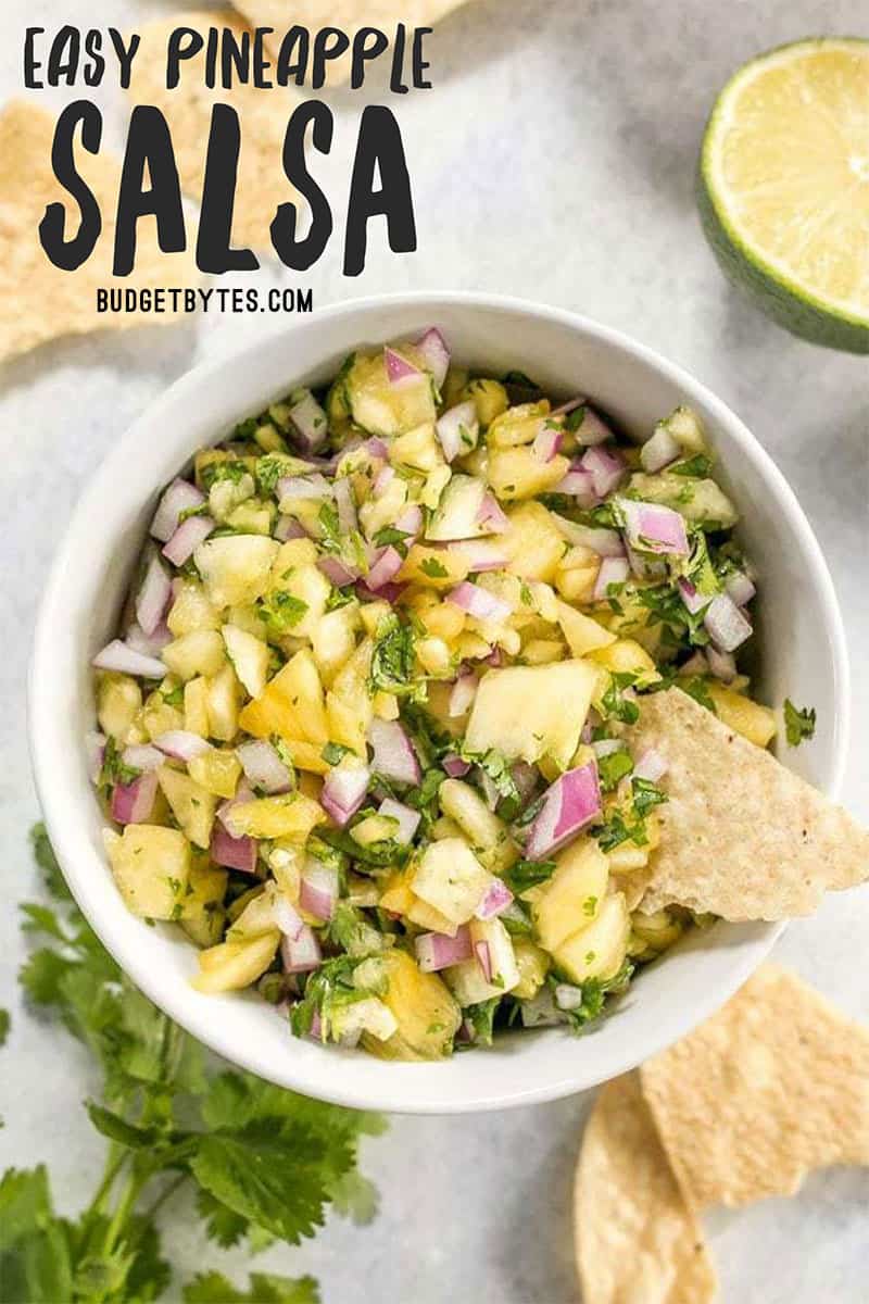 Overhead view of a bowl full of easy pineapple salsa, with chips, cilantro and limes on the side