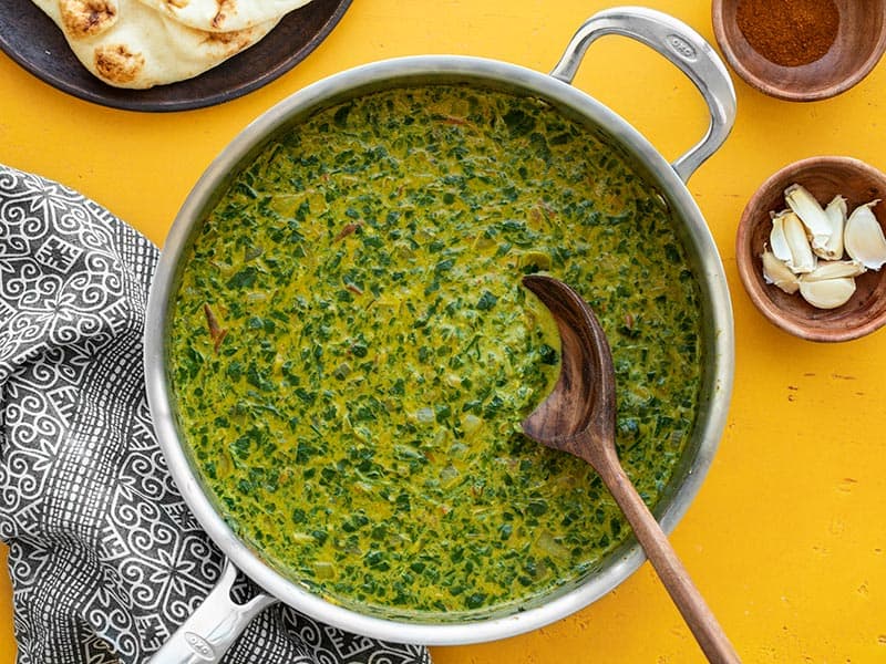 A skillet full of Indian Creamed Spinach with a wooden spoon in the center